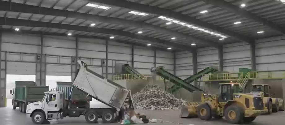Incoming waste being tipped from a truck onto the receiving floor, with a wheel loader and picking line in the background
